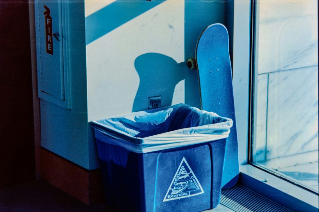 Blue trash can and skateboard by a window