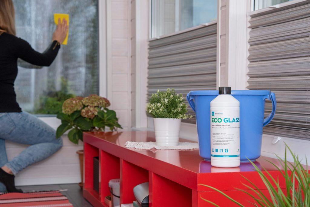 A woman sitting on a window sill cleaning a window